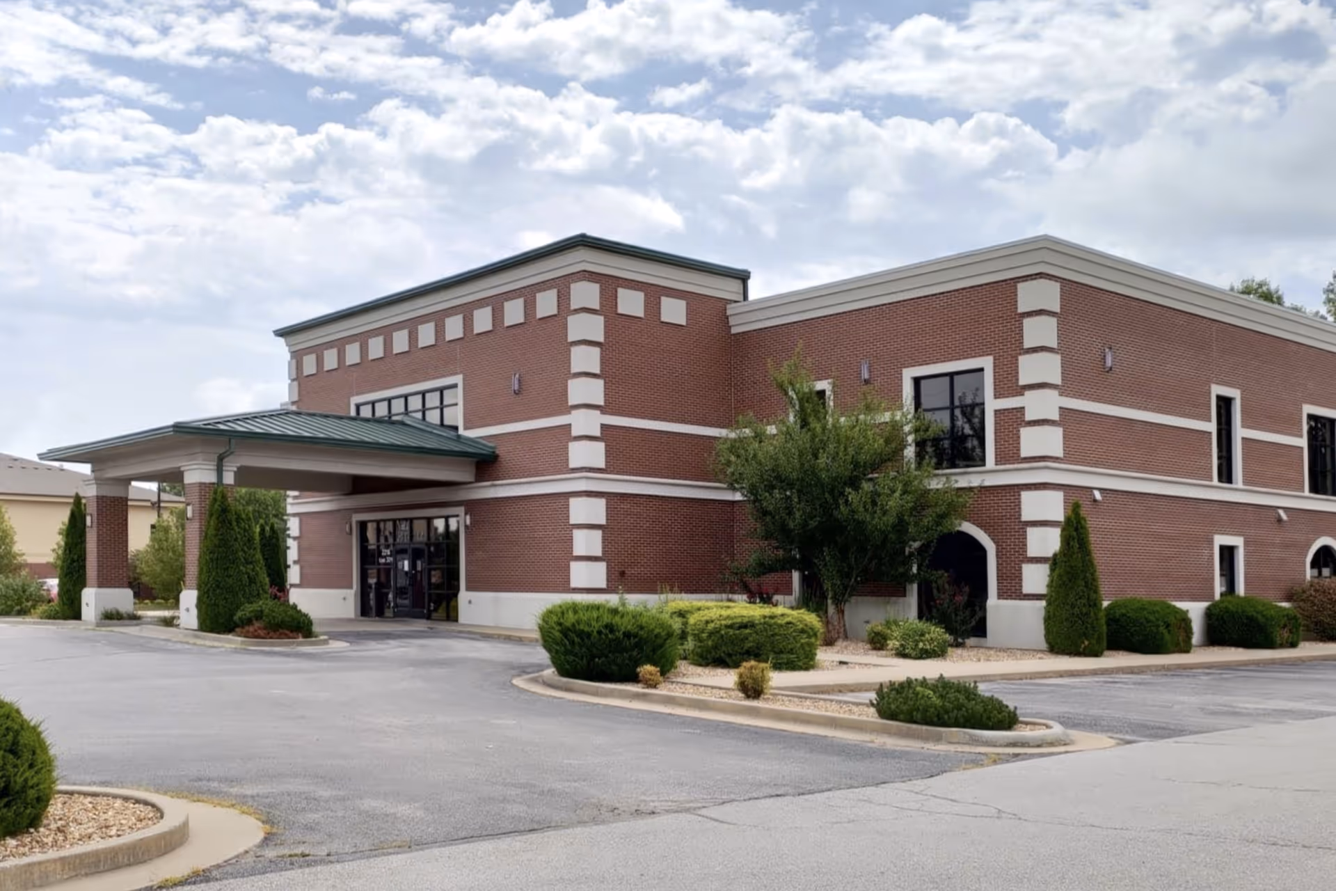 Brick senior living facility exterior with entrance, shrubs, and a parking lot.