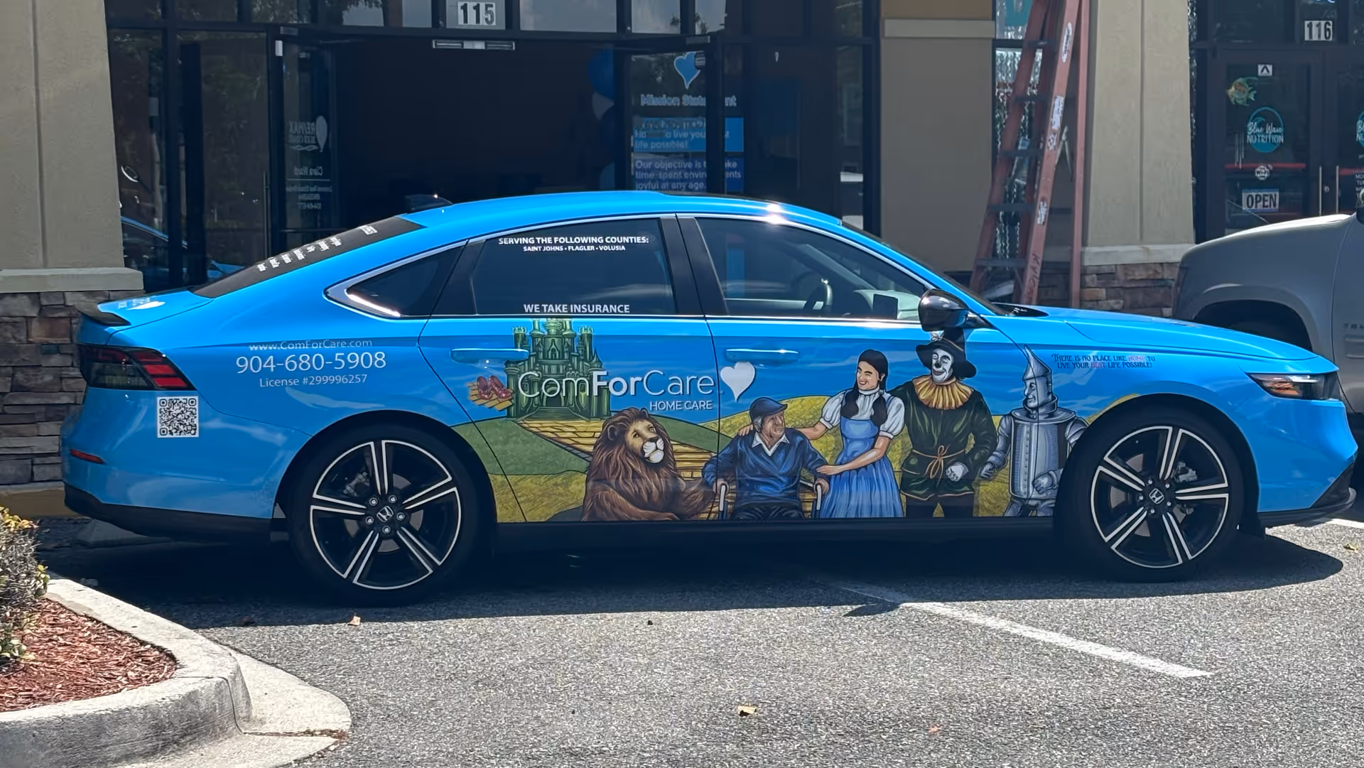 Blue promotion car with ComForCare Home Care mural parked outside storefront.