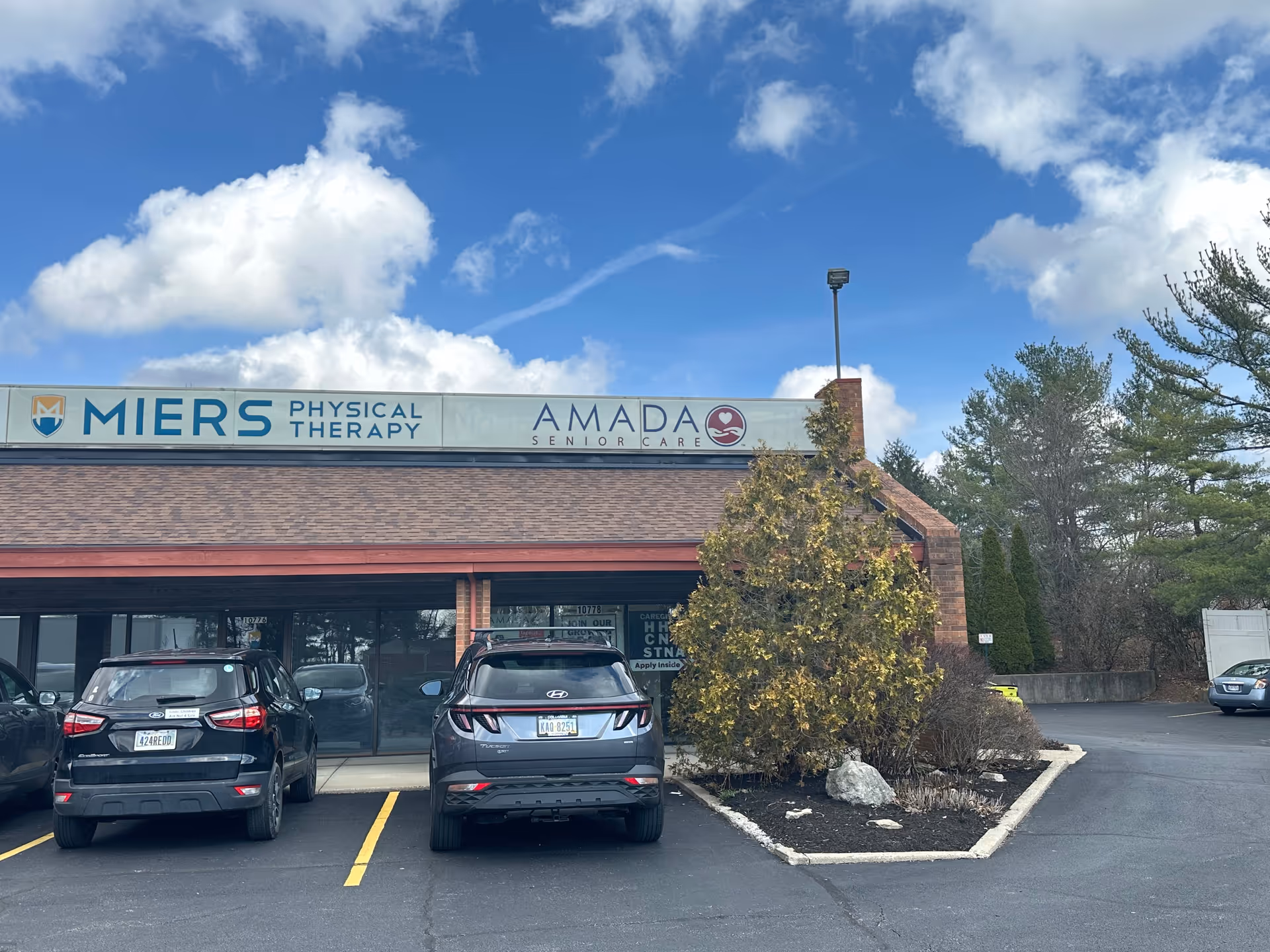 Brick storefront with Amada Senior Care and Miers Physical Therapy signage, parked cars in front.