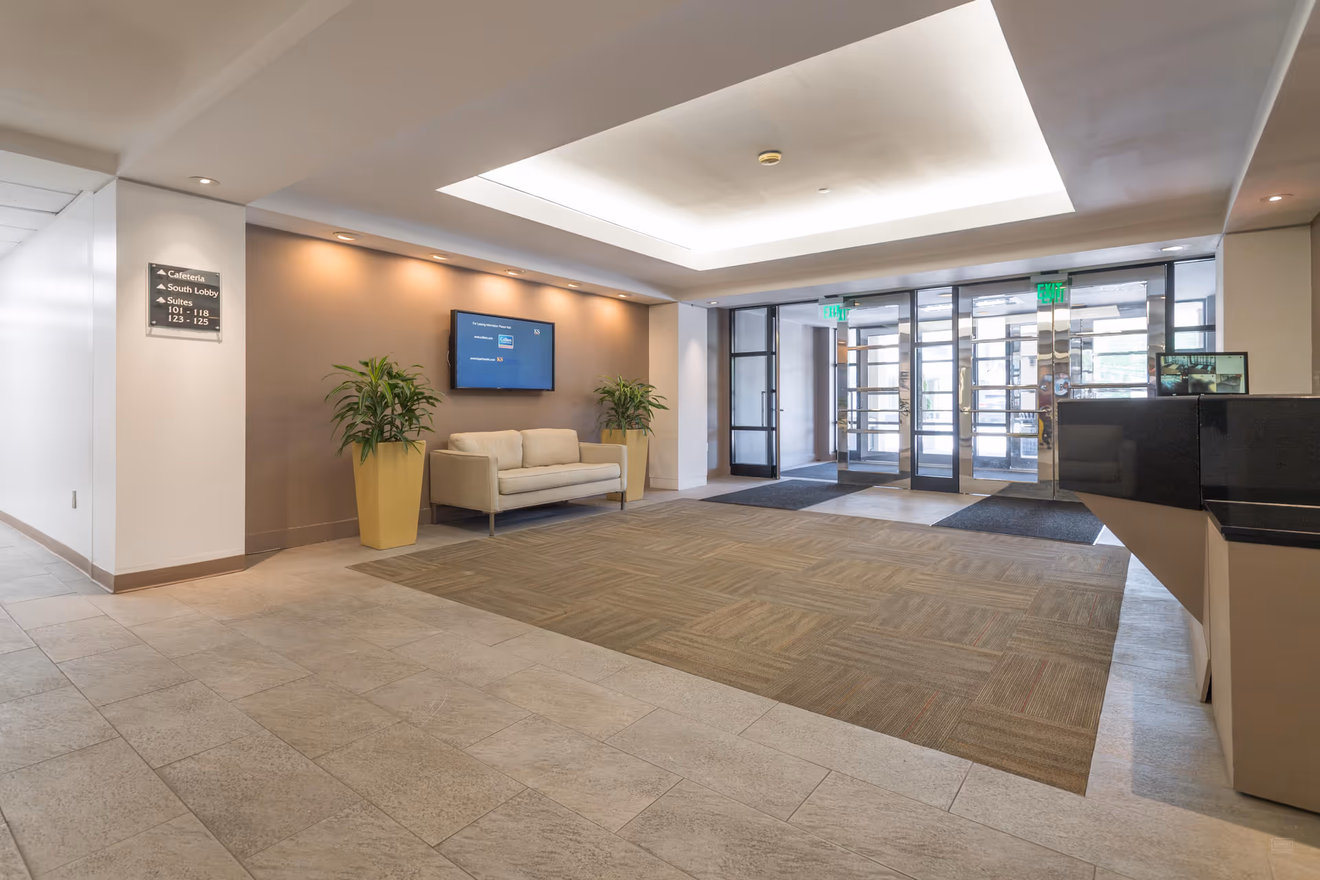 Modern senior-living lobby with beige sofa, potted plants, TV, and glass entry doors.
