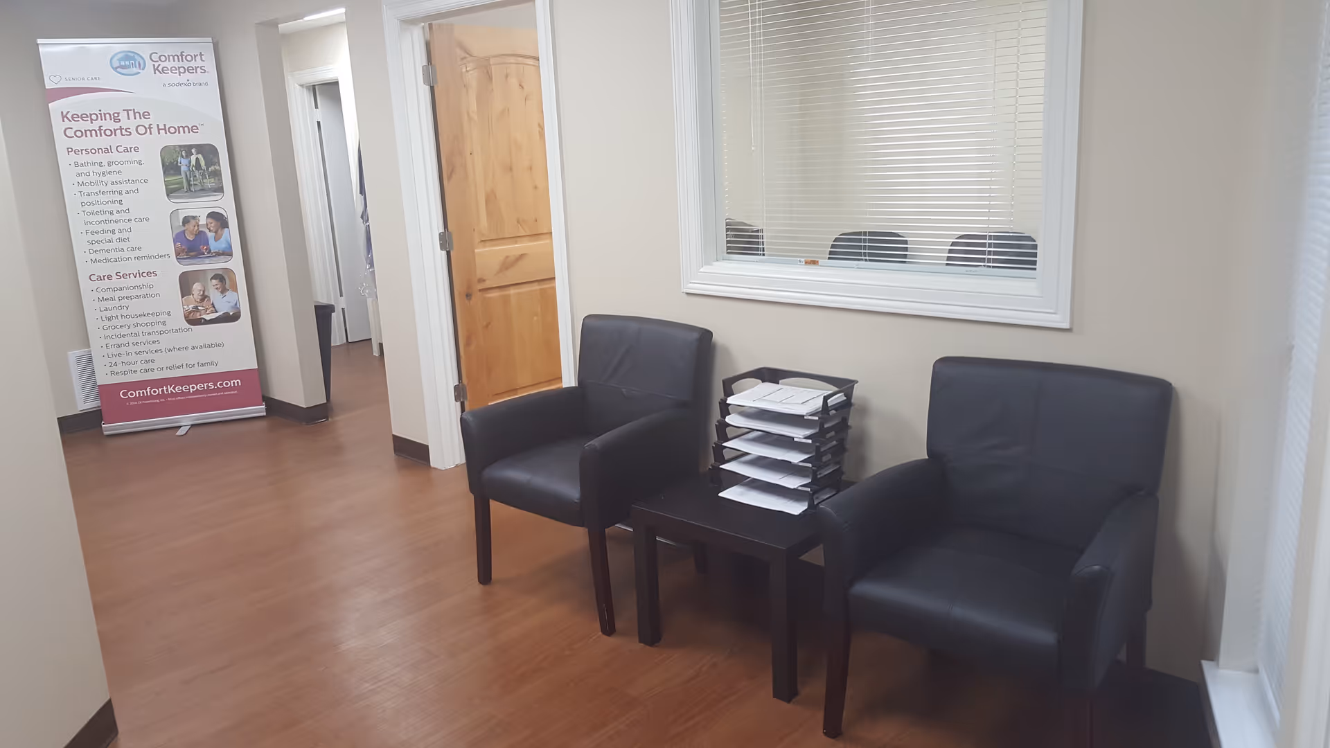 Waiting area with two black chairs, a small table stacked with papers, and a brochure stand.