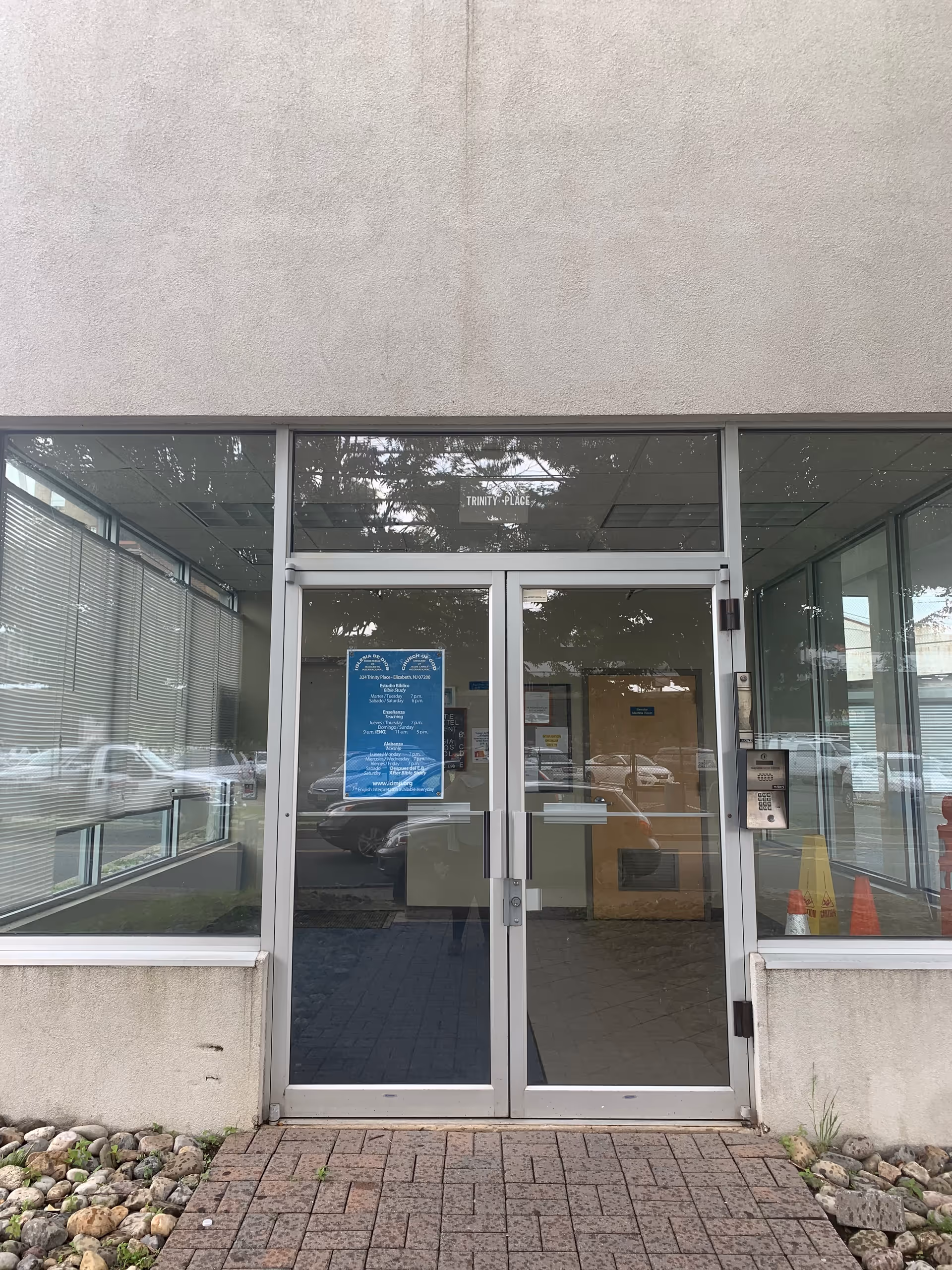 Glass double doors framed by a concrete building, with a blue sign at the entrance.