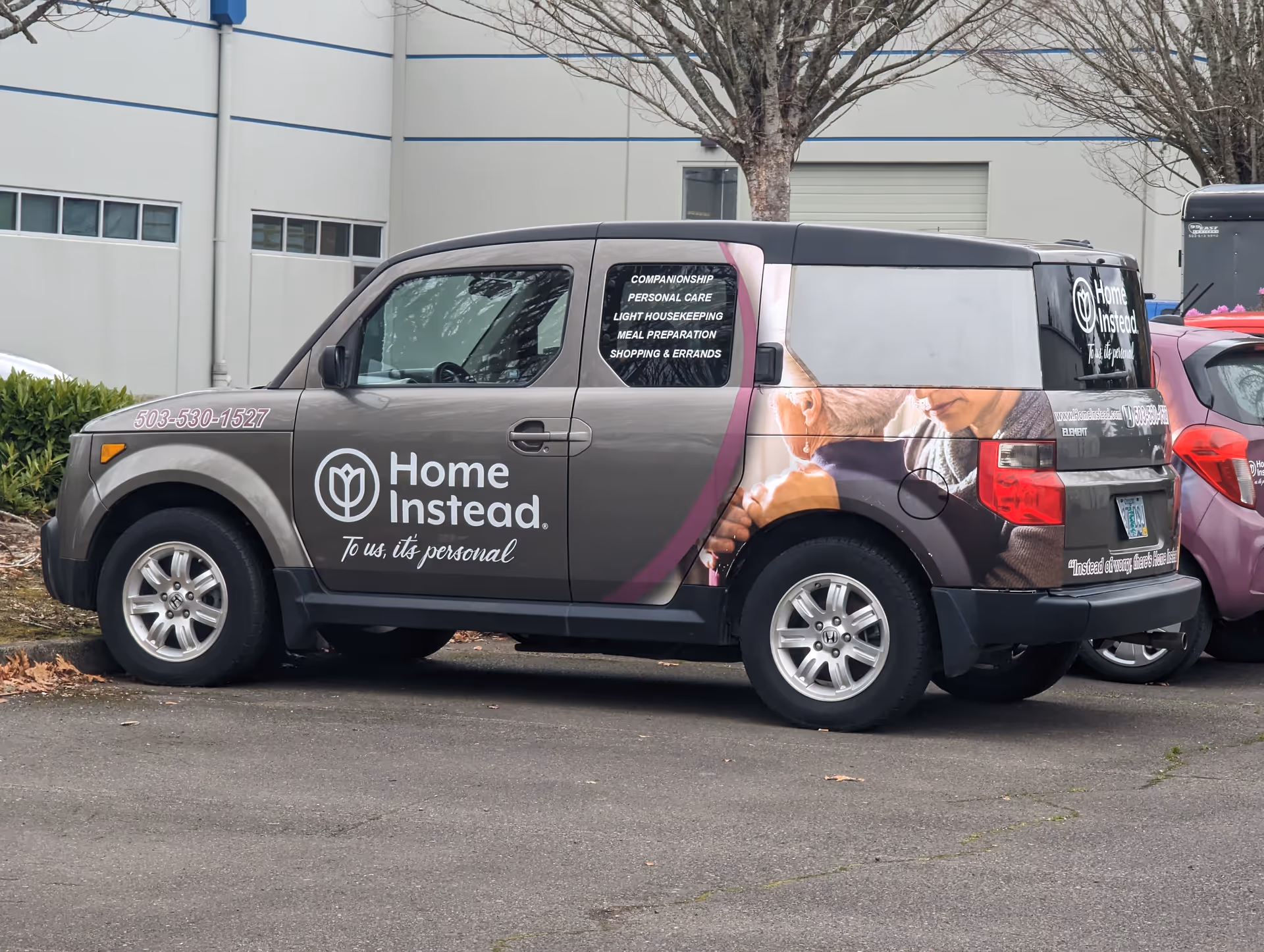 A Home Instead branded van parked in a lot beside a gray building.