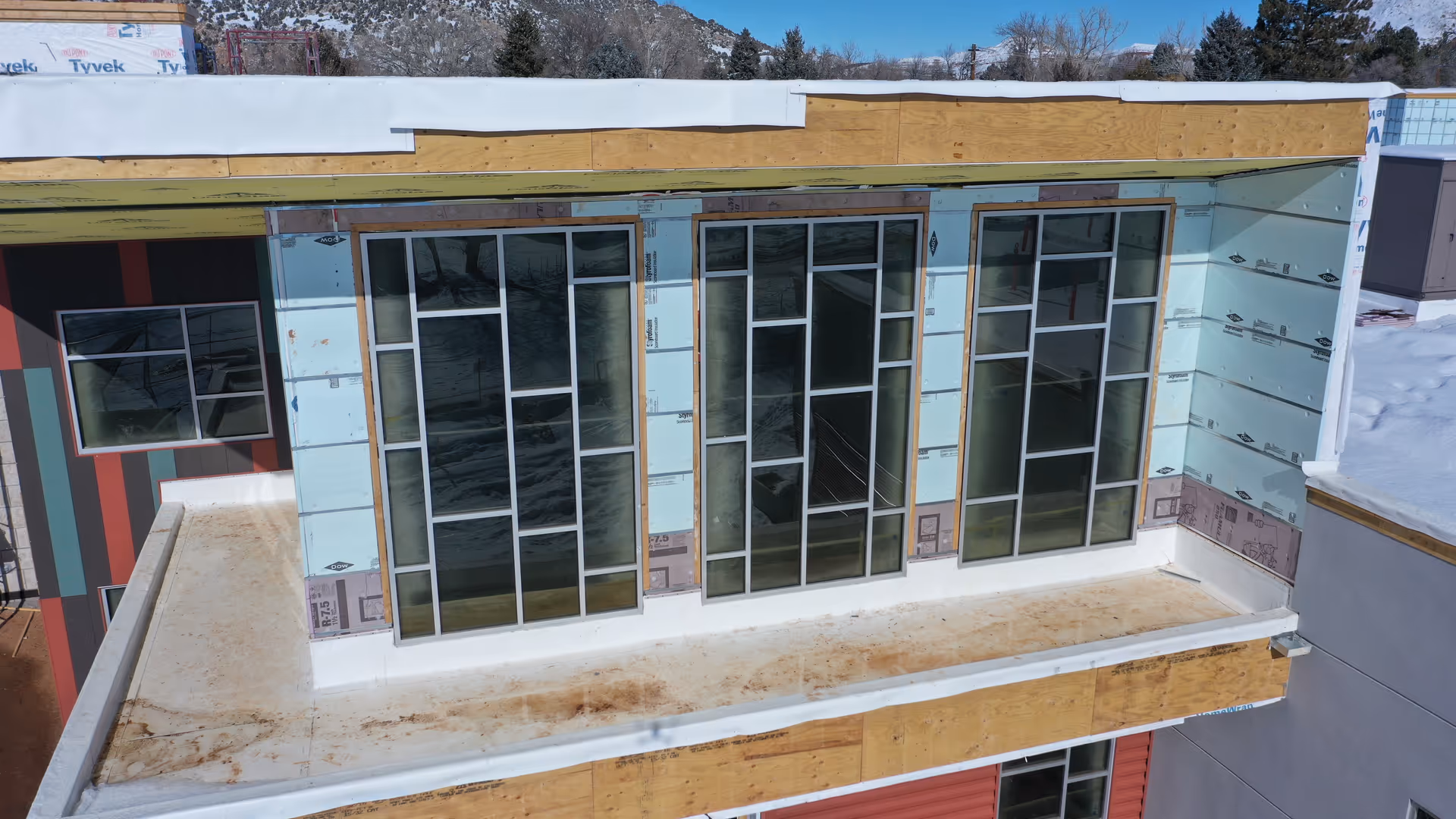 Exterior of a modern building under construction with large glass doors and exposed framing.