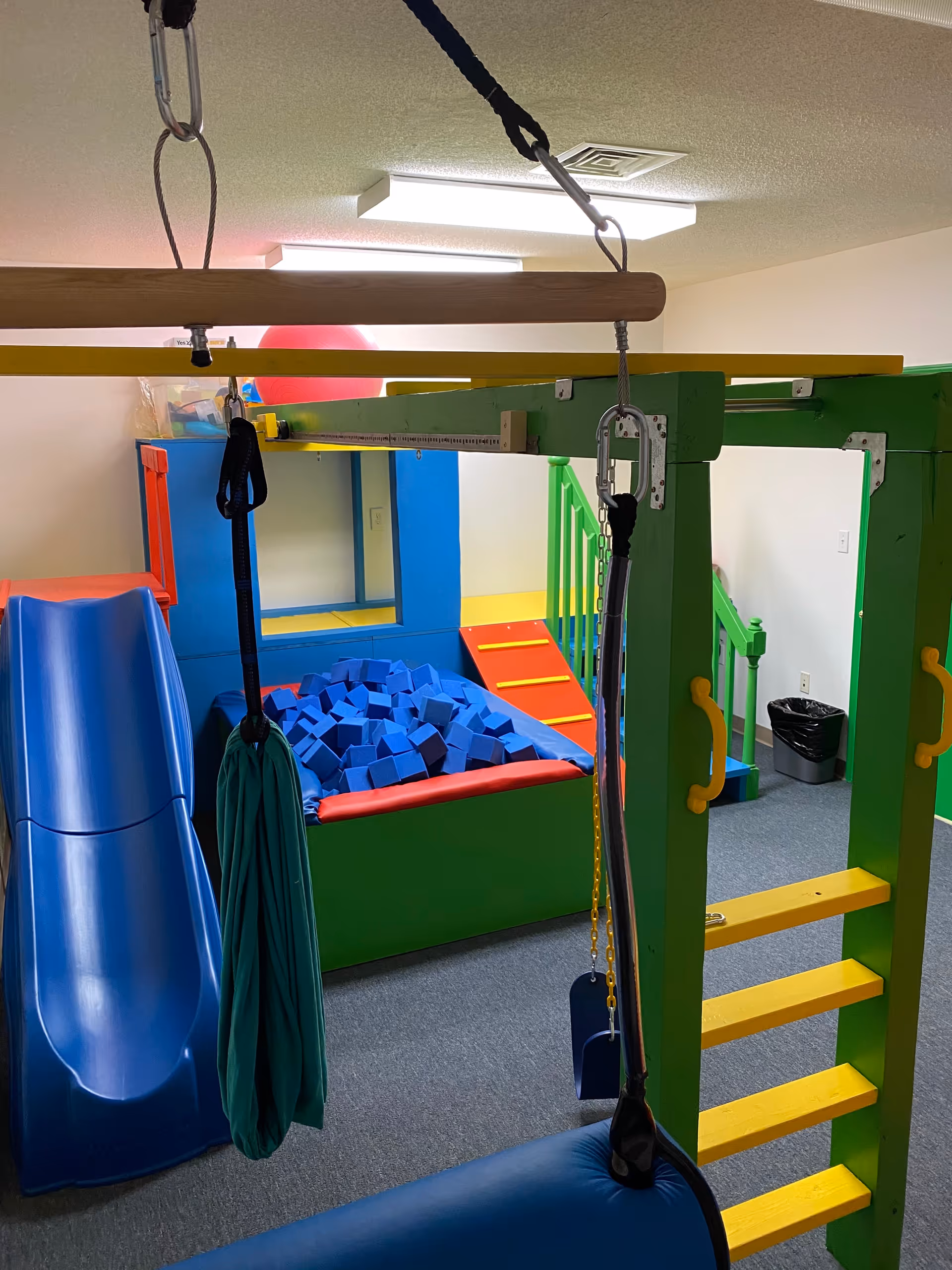 Colorful indoor therapy space with play equipment, foam pit, and climbing structures.