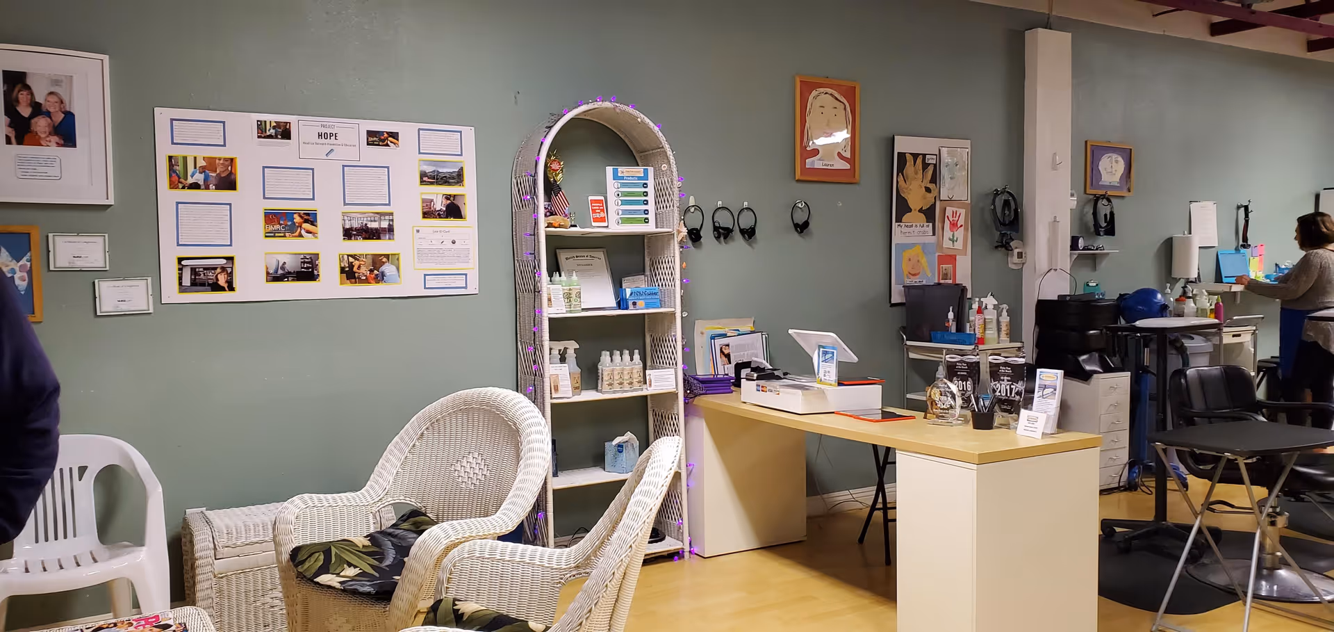 Interior lounge with wicker chairs, reception desk, shelves, and a staff member in the background.