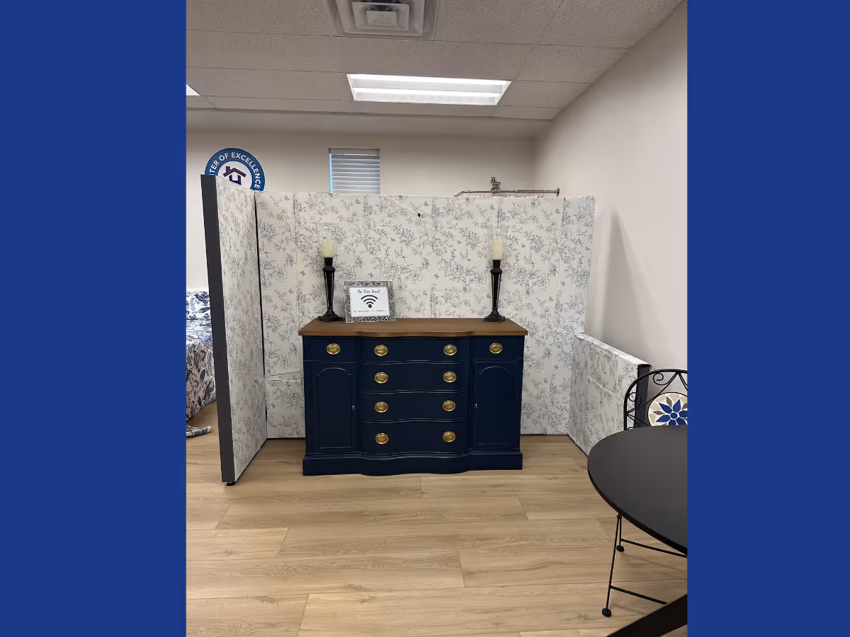 Blue dresser against a floral divider in a tidy senior living interior with a round table.