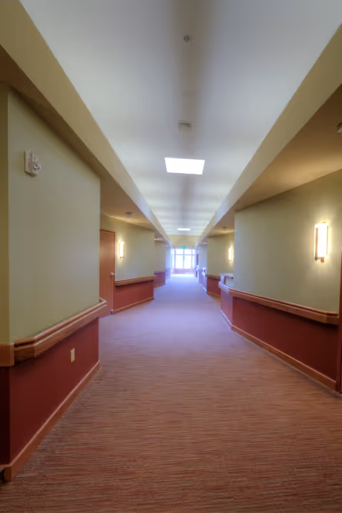 A long, empty hallway with green walls, carpet, and wall sconces.