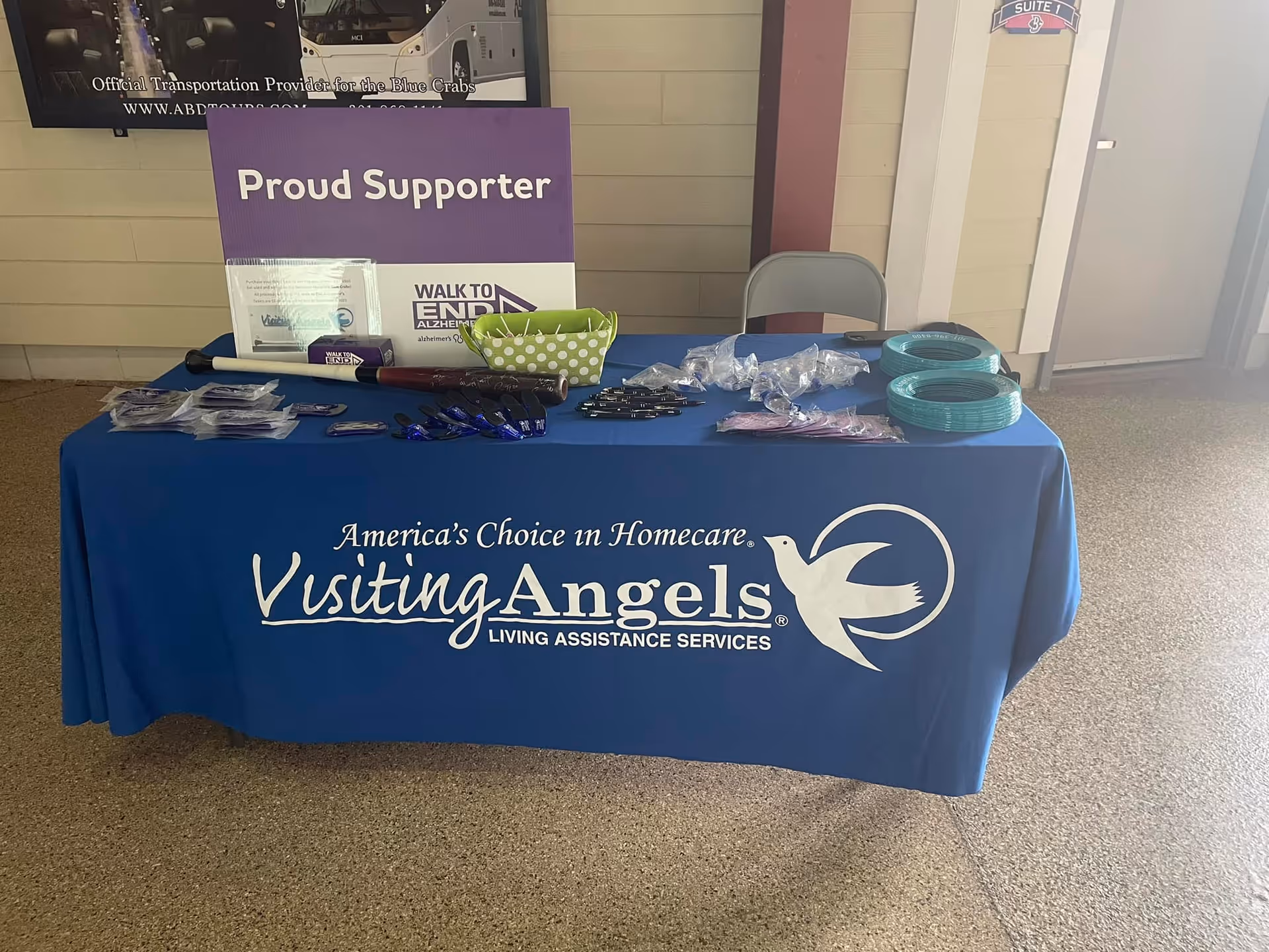 Blue Visiting Angels promotional table labeled Proud Supporter sits in an interior lobby.
