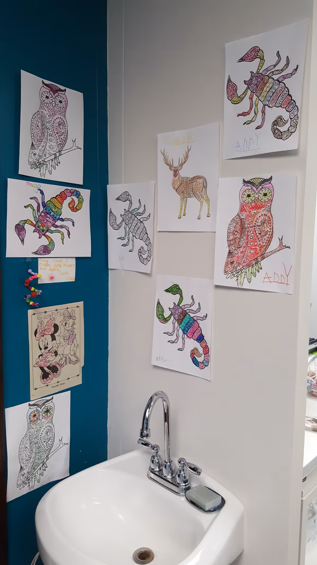 Interior bathroom sink area with colorful kids' drawings taped to the walls.
