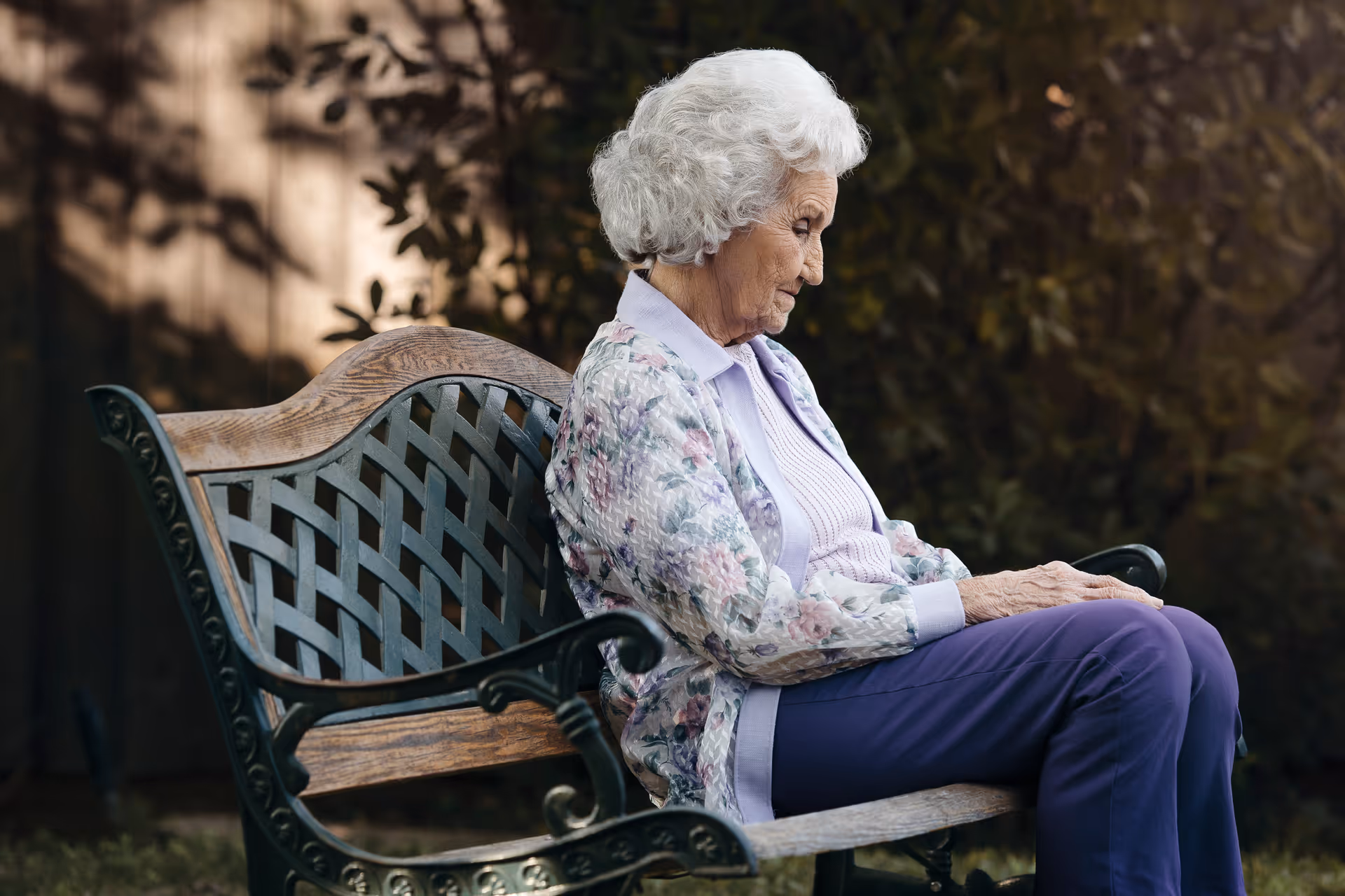 An elderly woman sits on a decorative park bench outdoors.