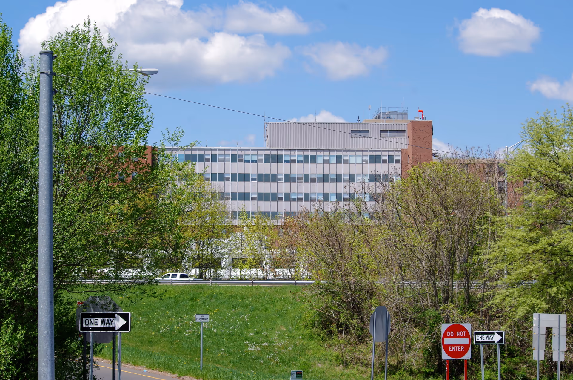 Exterior view of Middlesex Hospital with trees, a grassy foreground, and street signs.