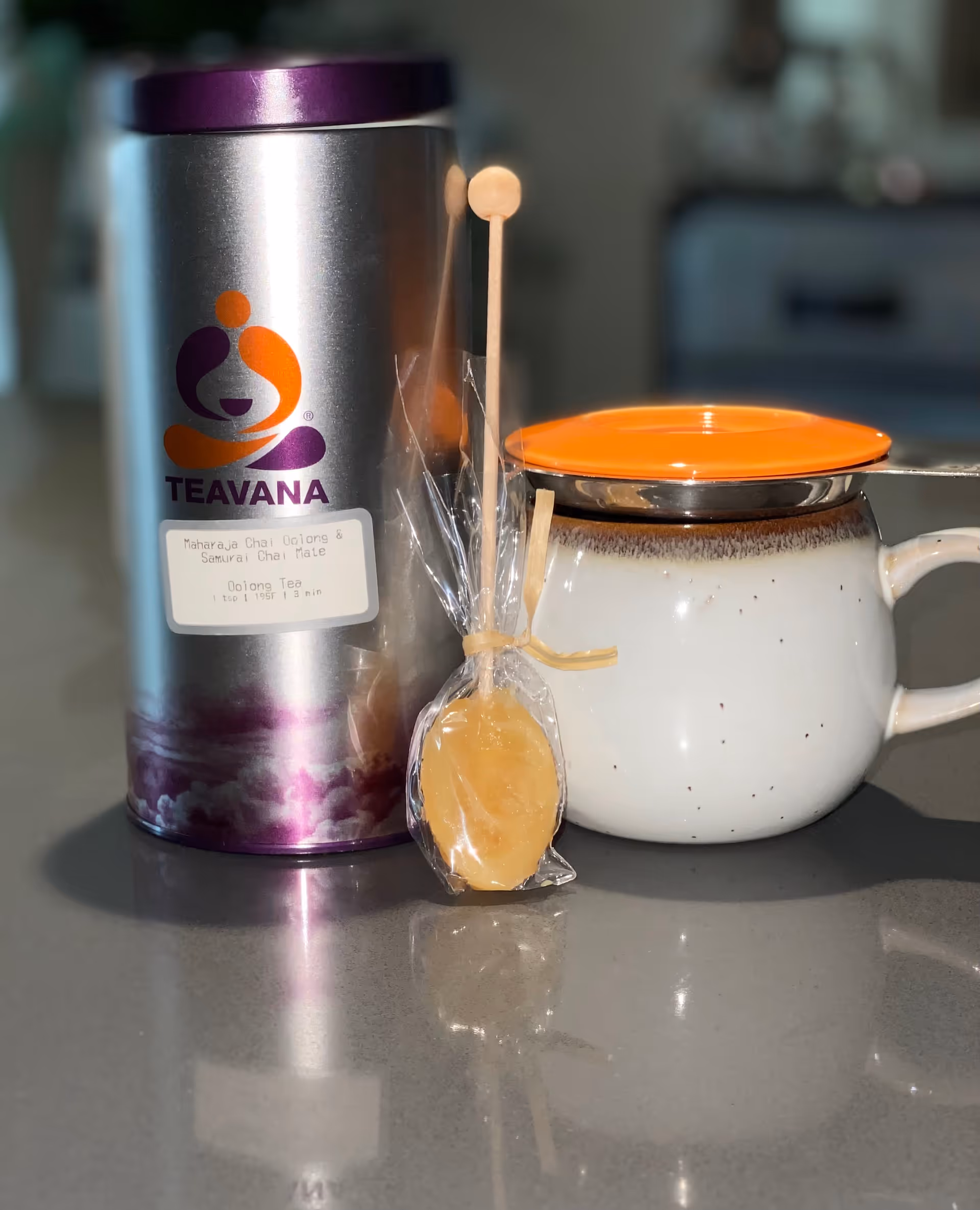 Close-up of a Teavana tea tin beside a white mug on a kitchen counter.