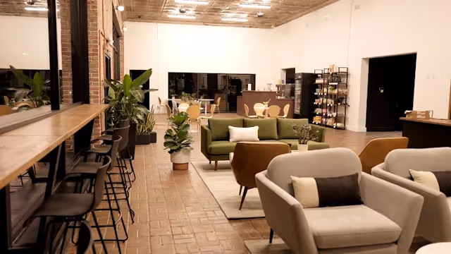 Spacious senior living lounge with a green sofa, neutral chairs, bar counter, and plants.
