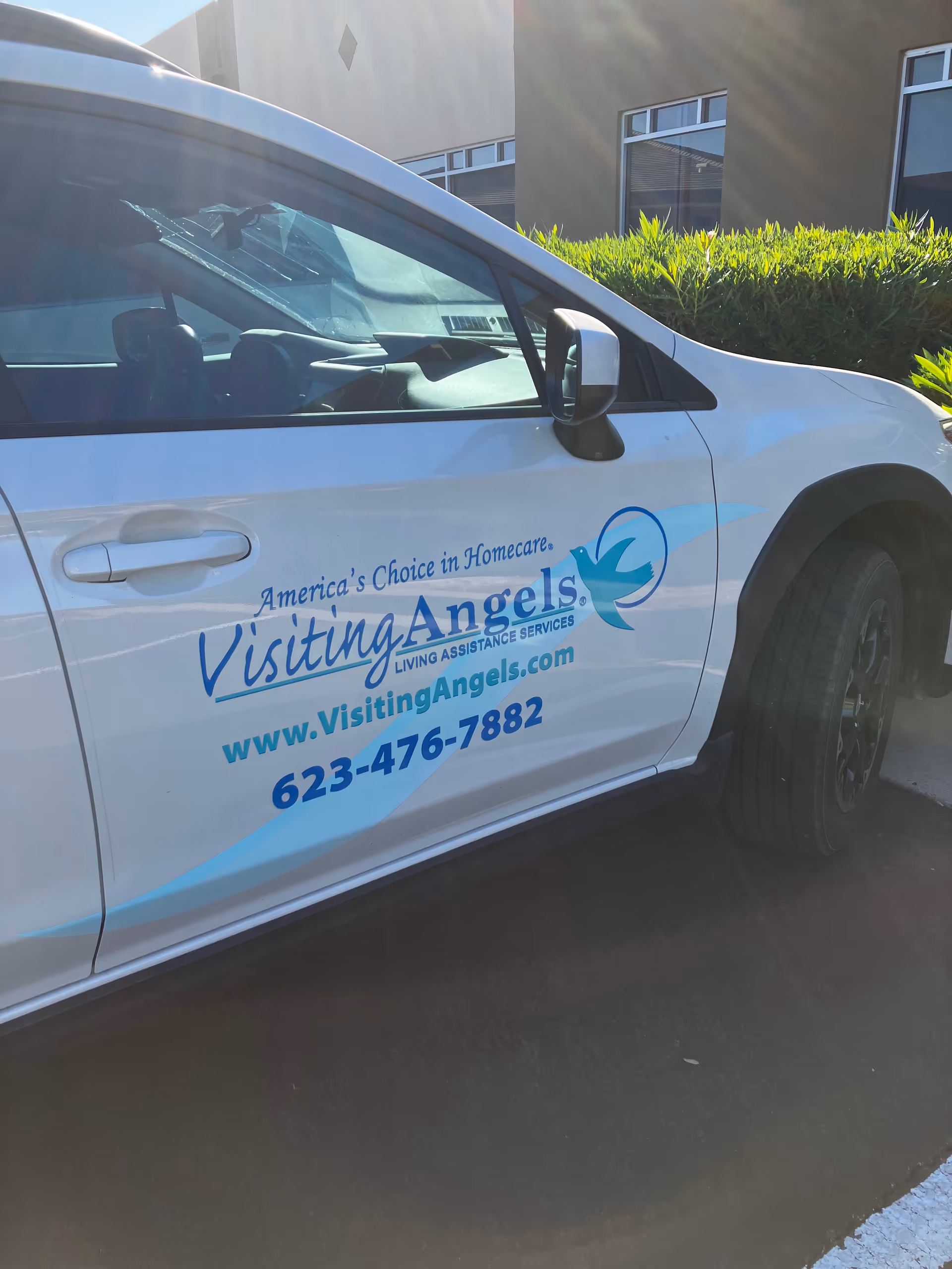 White Visiting Angels van parked outside a facility with green shrubbery.