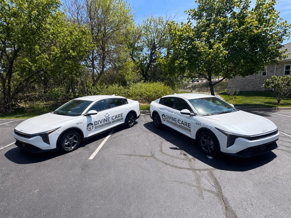 Two white Divine Care branded vehicles parked in a lot beside trees.