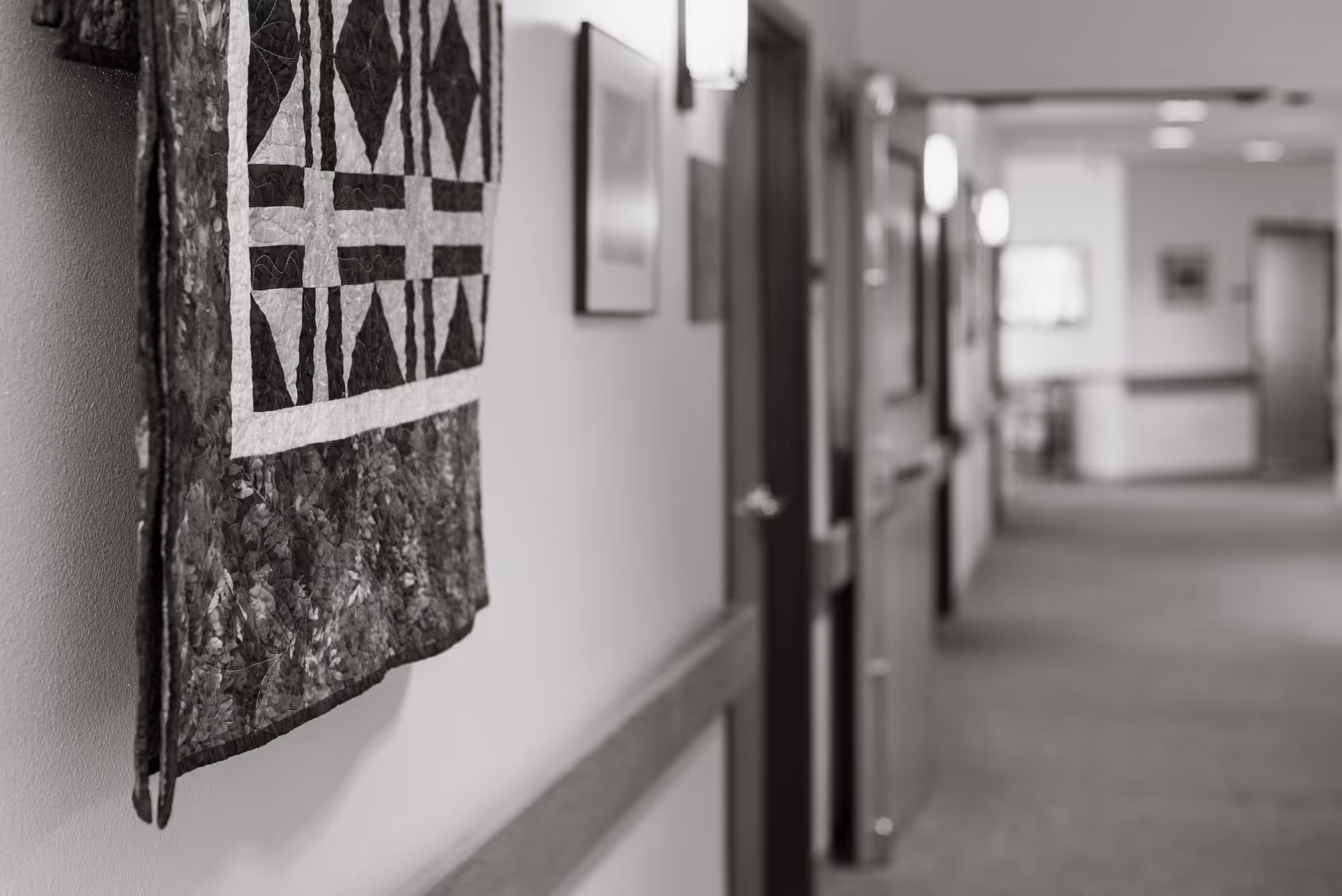 Black-and-white hallway in a senior living facility with a quilt hanging on the wall.
