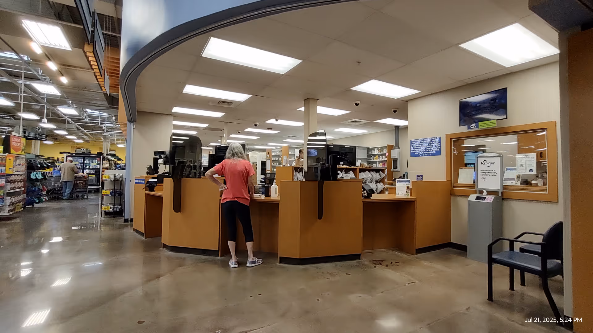 Inside a Kroger Pharmacy, a curved wooden service counter with staff and customers.