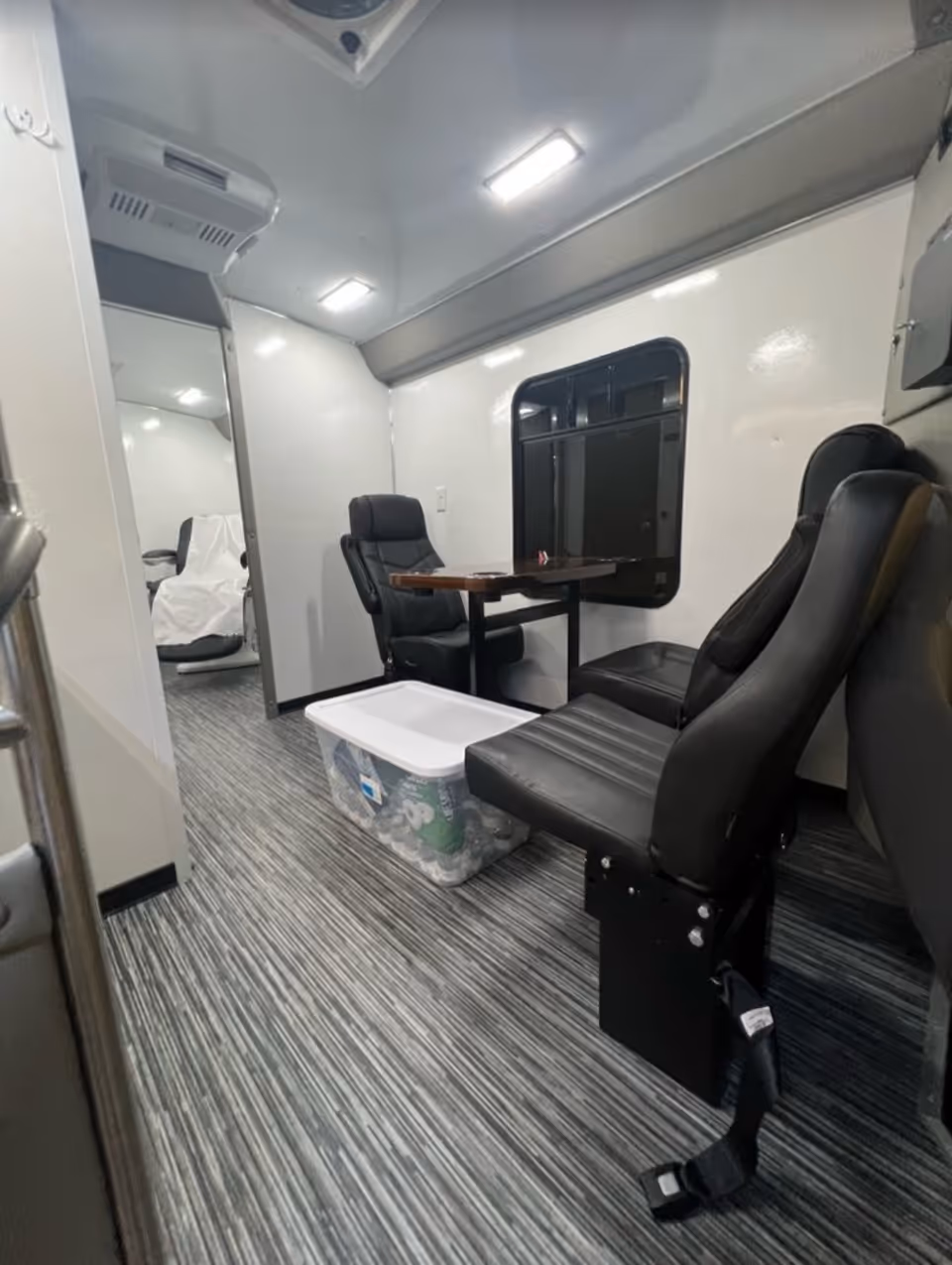 Interior of a mobile medical care unit with black seats, table, and storage bin.