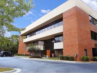 Brick office-style building exterior with large windows and a parking lot.