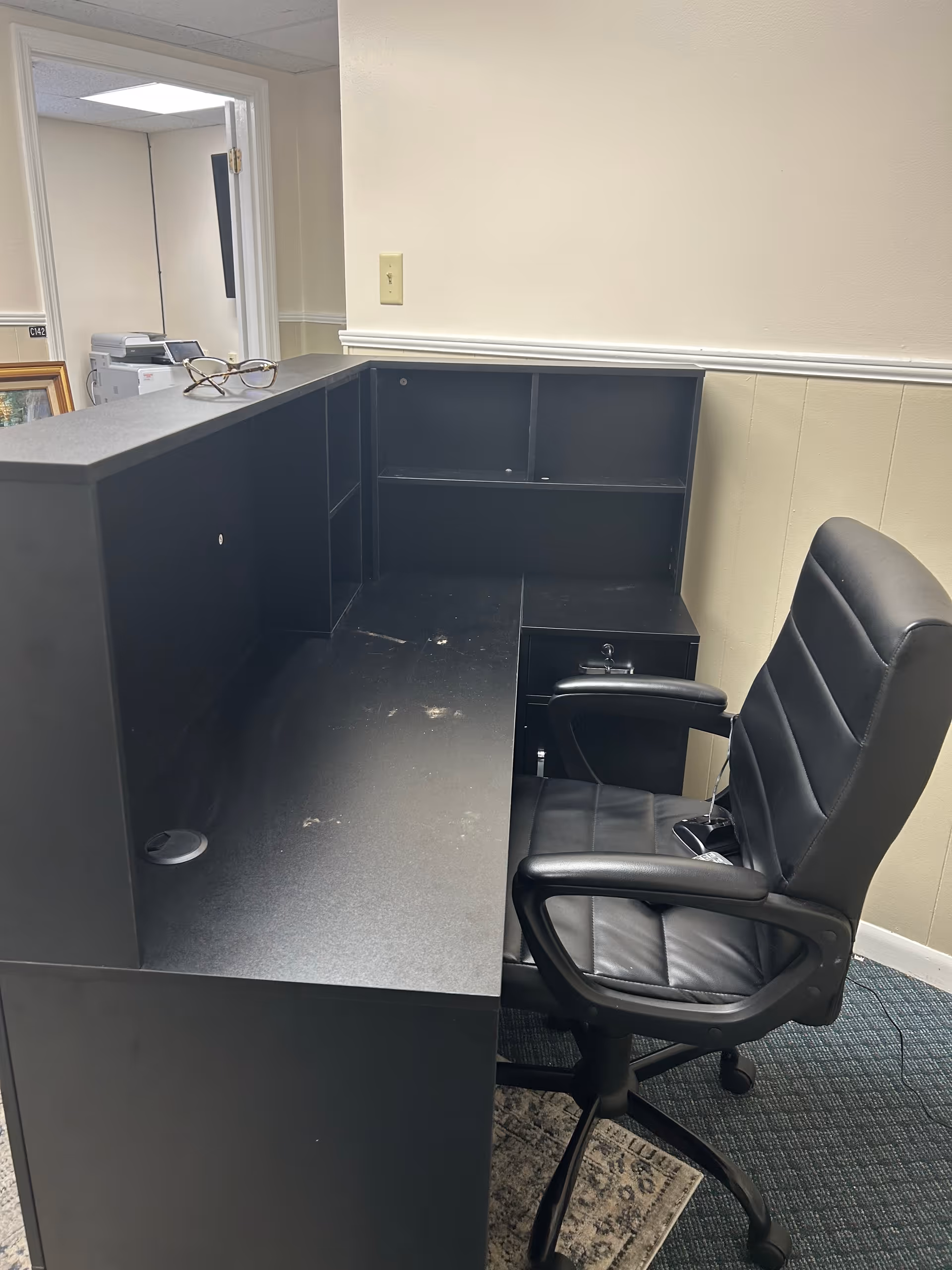 An L-shaped black desk with a swivel chair in a small office area.