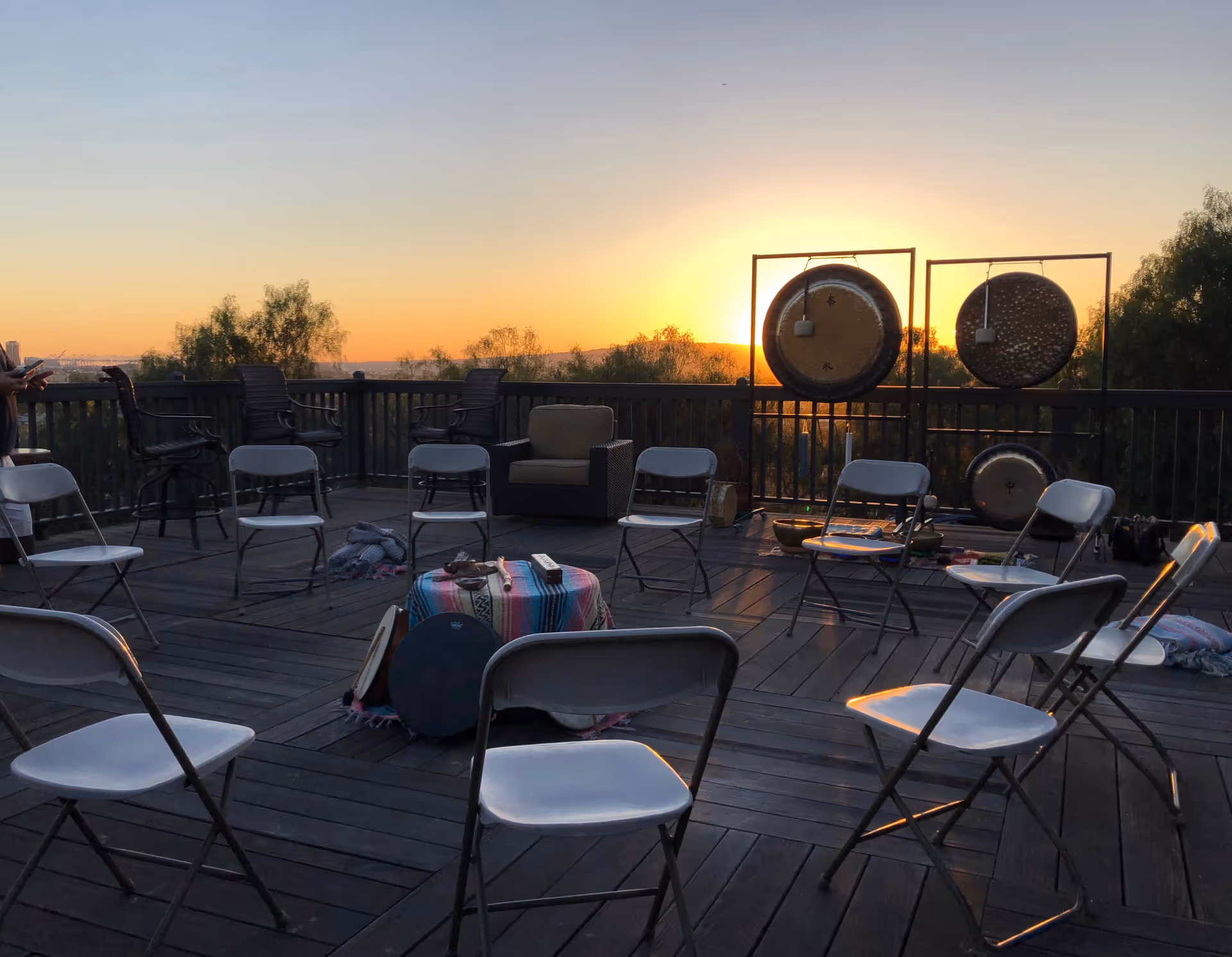 Outdoor rooftop deck with folding chairs and large percussion gongs at sunset.