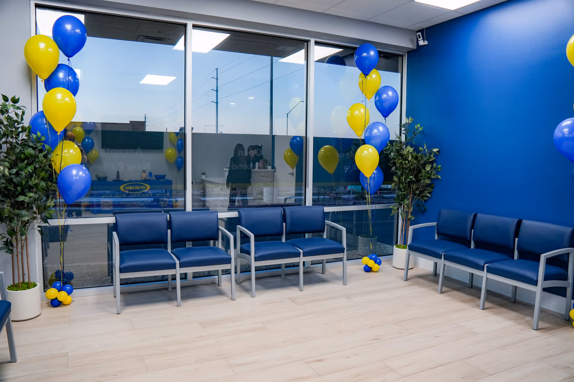 Blue-walled waiting area with blue chairs, glass windows, and balloons.