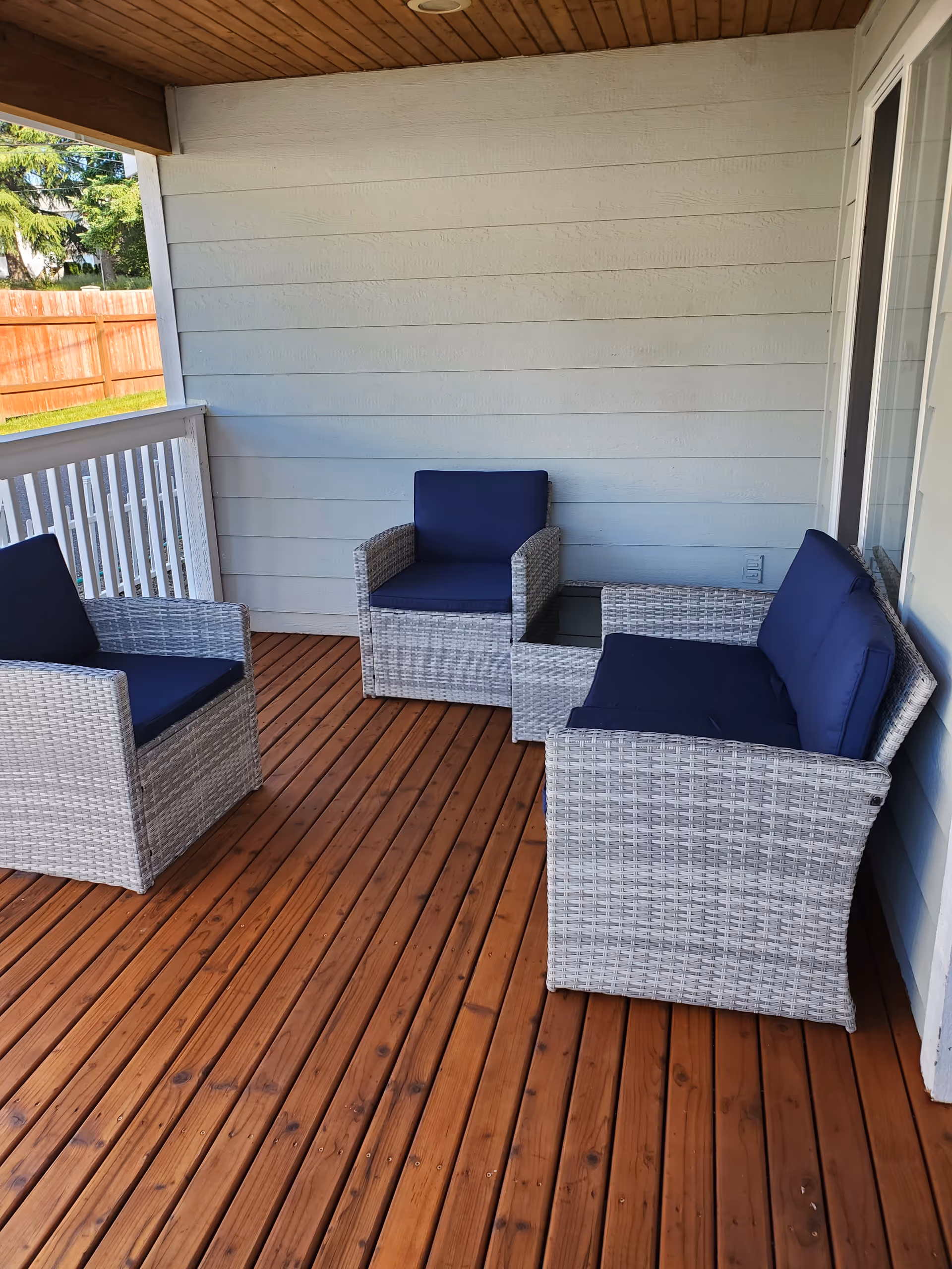 Outdoor balcony with four wicker chairs and a glass table, navy cushions on wood deck.