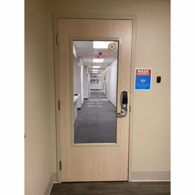 Interior hallway with a wooden door featuring a glass panel and Mercy Health Compassus branding.