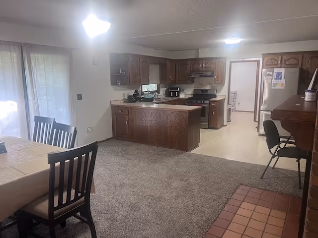 Open kitchen and dining area in a senior living facility with wooden cabinets and island.