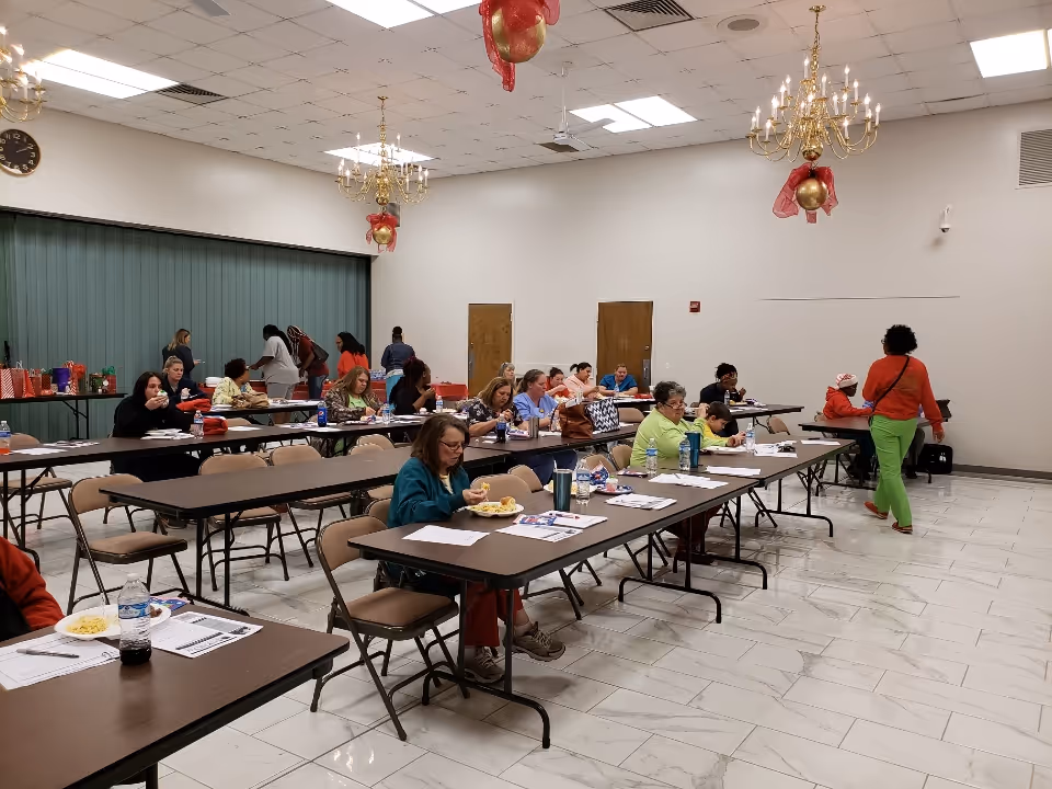 Interior view of a communal dining hall with residents eating at long tables.