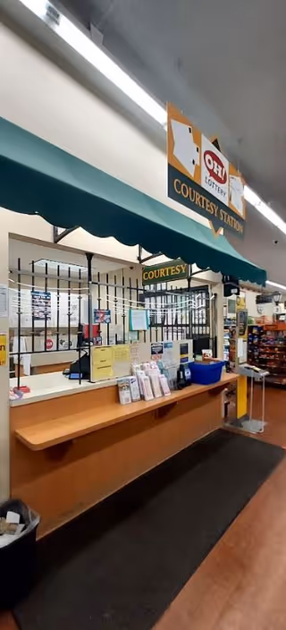 Inside a Discount Drug Mart, a checkout counter with a courtesy station sign and green awning.