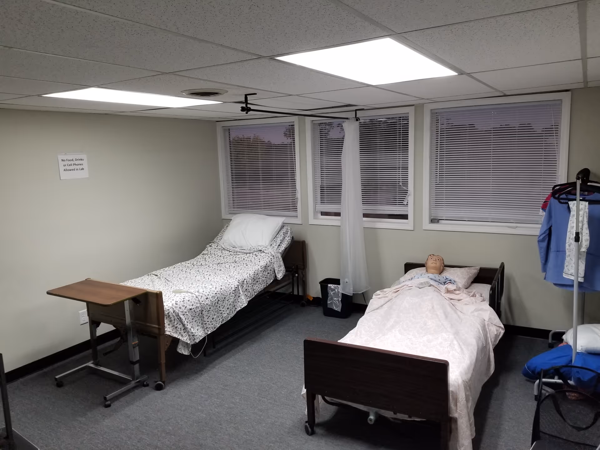 Two hospital beds in a small patient room with a medical mannequin.