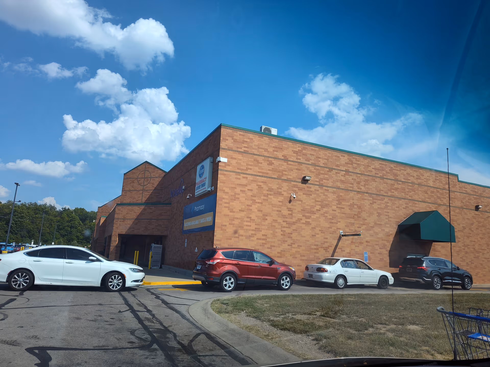 Exterior view of a Kroger Pharmacy building with parked cars and a blue sky.