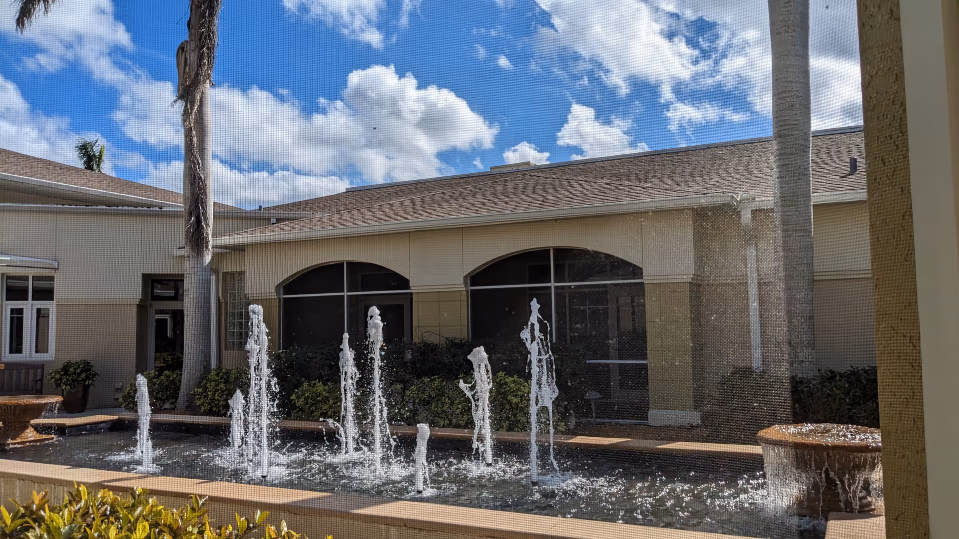 Exterior view of Hope Hospice courtyard with a rectangular fountain and palm trees.