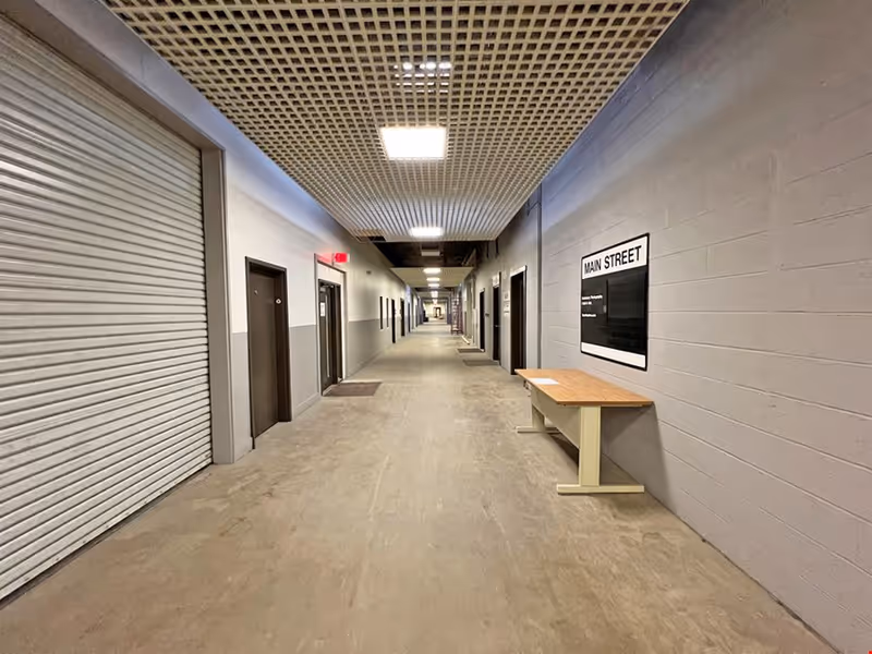 Long indoor hallway with doors on both sides and a wooden table against gray wall.