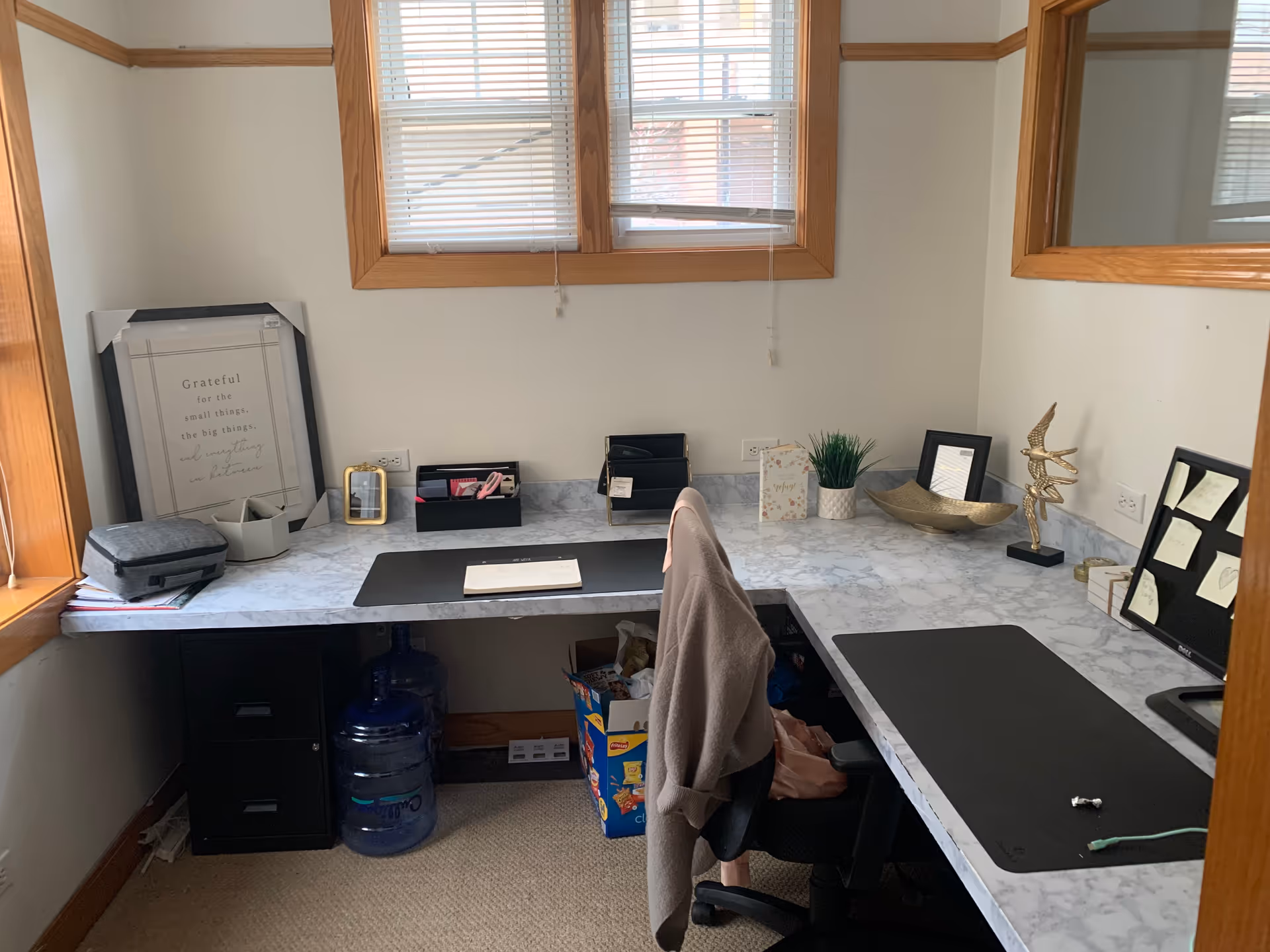 Corner home office with marble desk, chair, window view, and organization items.