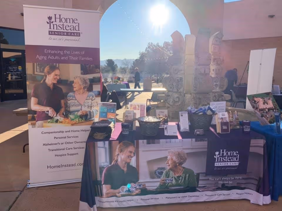 Outdoor Home Instead booth with banner, table, brochures, and a few people in background.