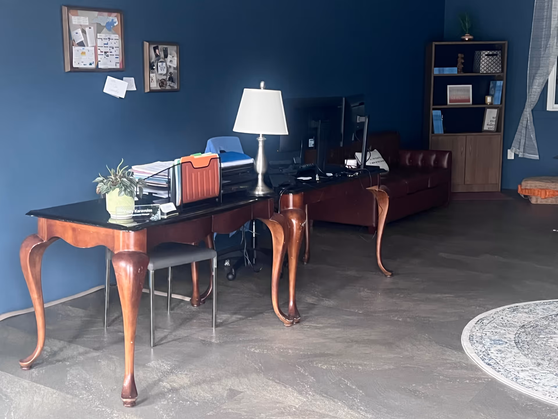 Blue-walled common area with a long wooden desk, lamp, shelves, a TV, and a leather sofa.