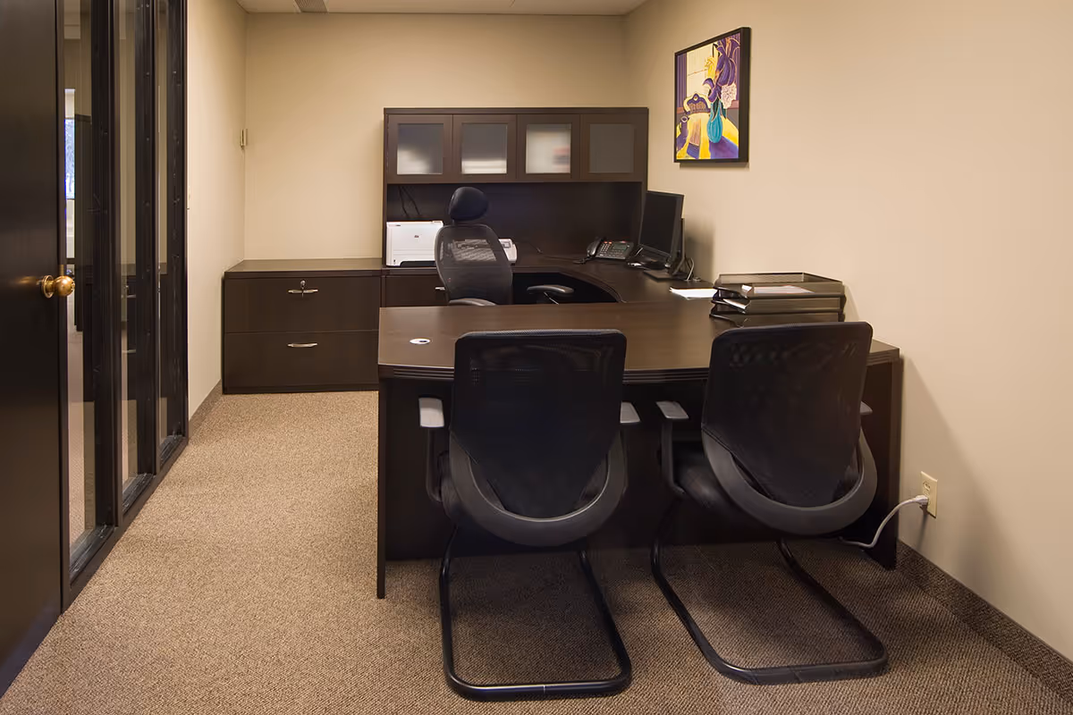 A dark wood office desk with chairs, cabinets, and a printer in a small corporate room.