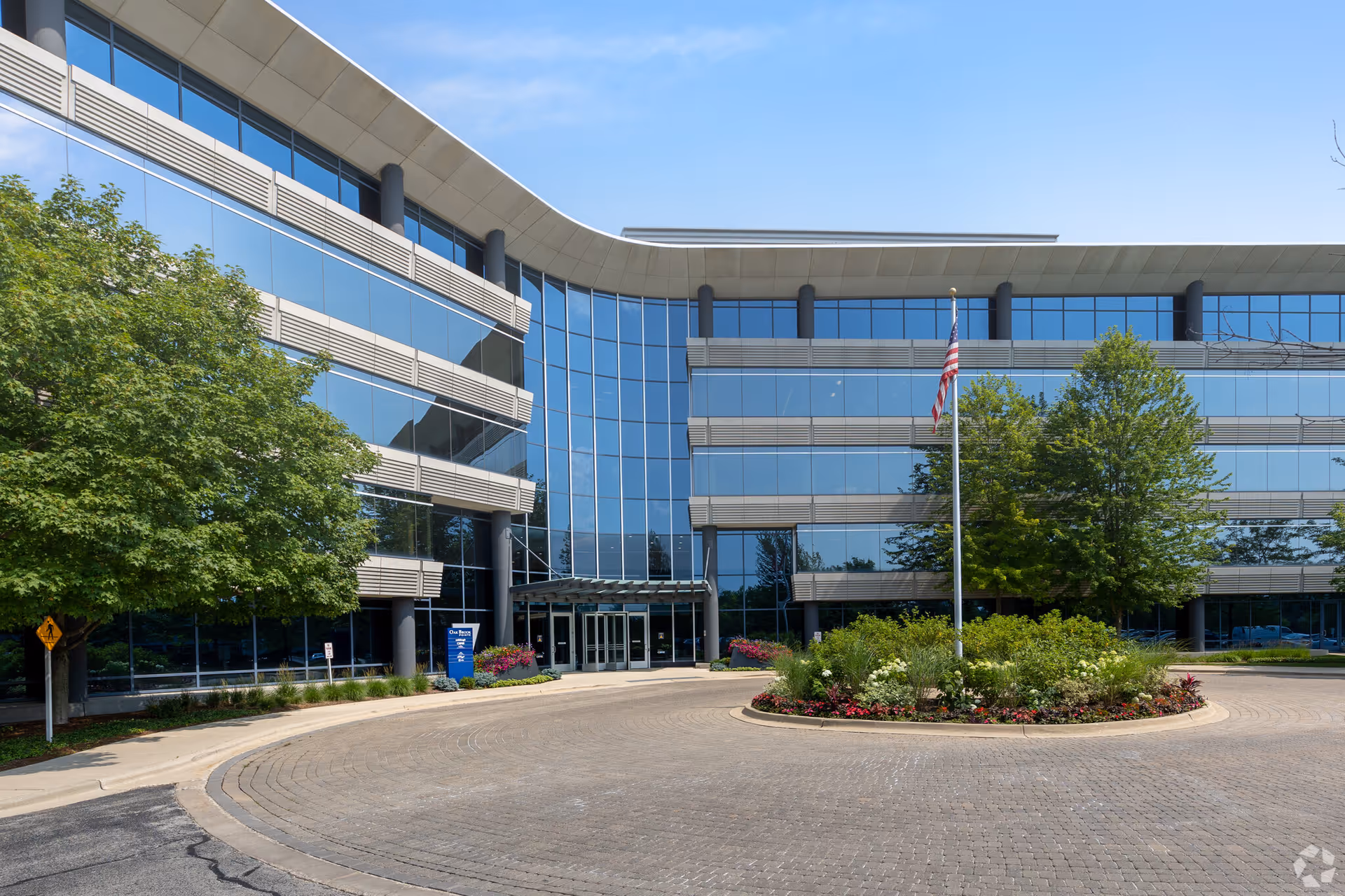 Modern glass-front office building with curved driveway and landscaped island.