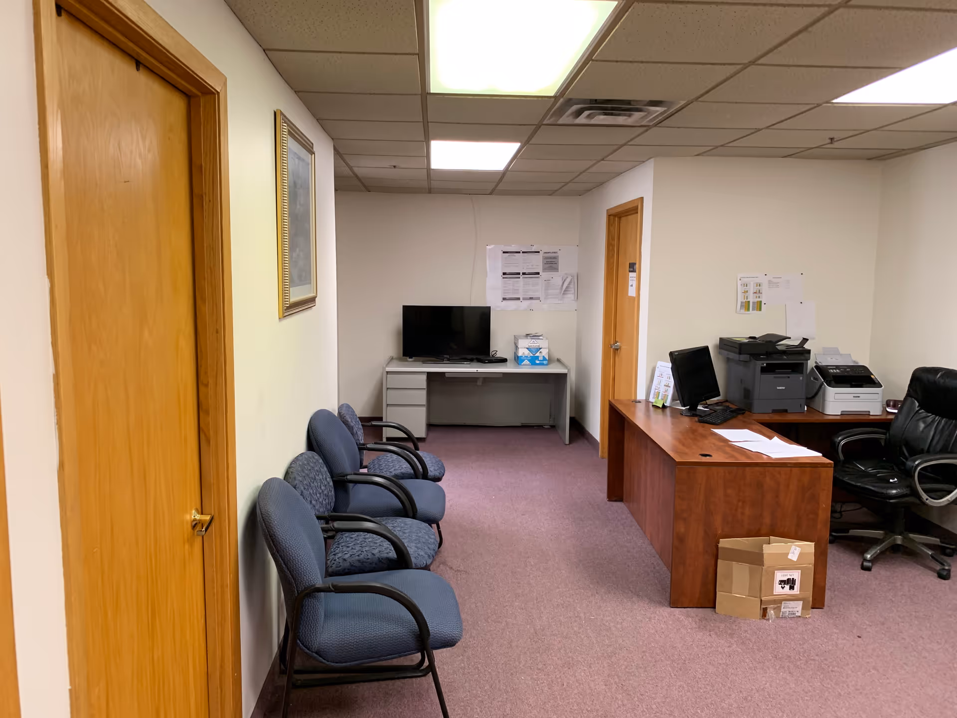 Office area in a senior facility with row of chairs, desk, computer, printer, and TV.