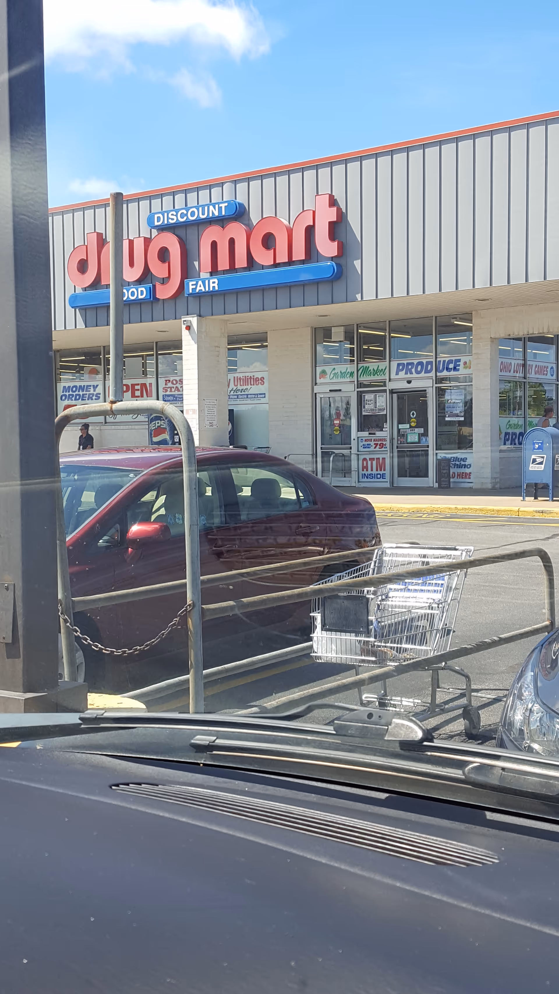 Front view of Discount Drug Mart storefront with a parked car and shopping cart.