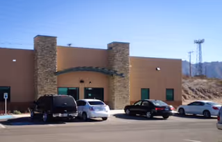 Front view of a beige building with stone pillars and a parking lot.