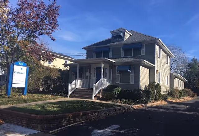 Two-story gray senior living building with a front porch and blue sign.