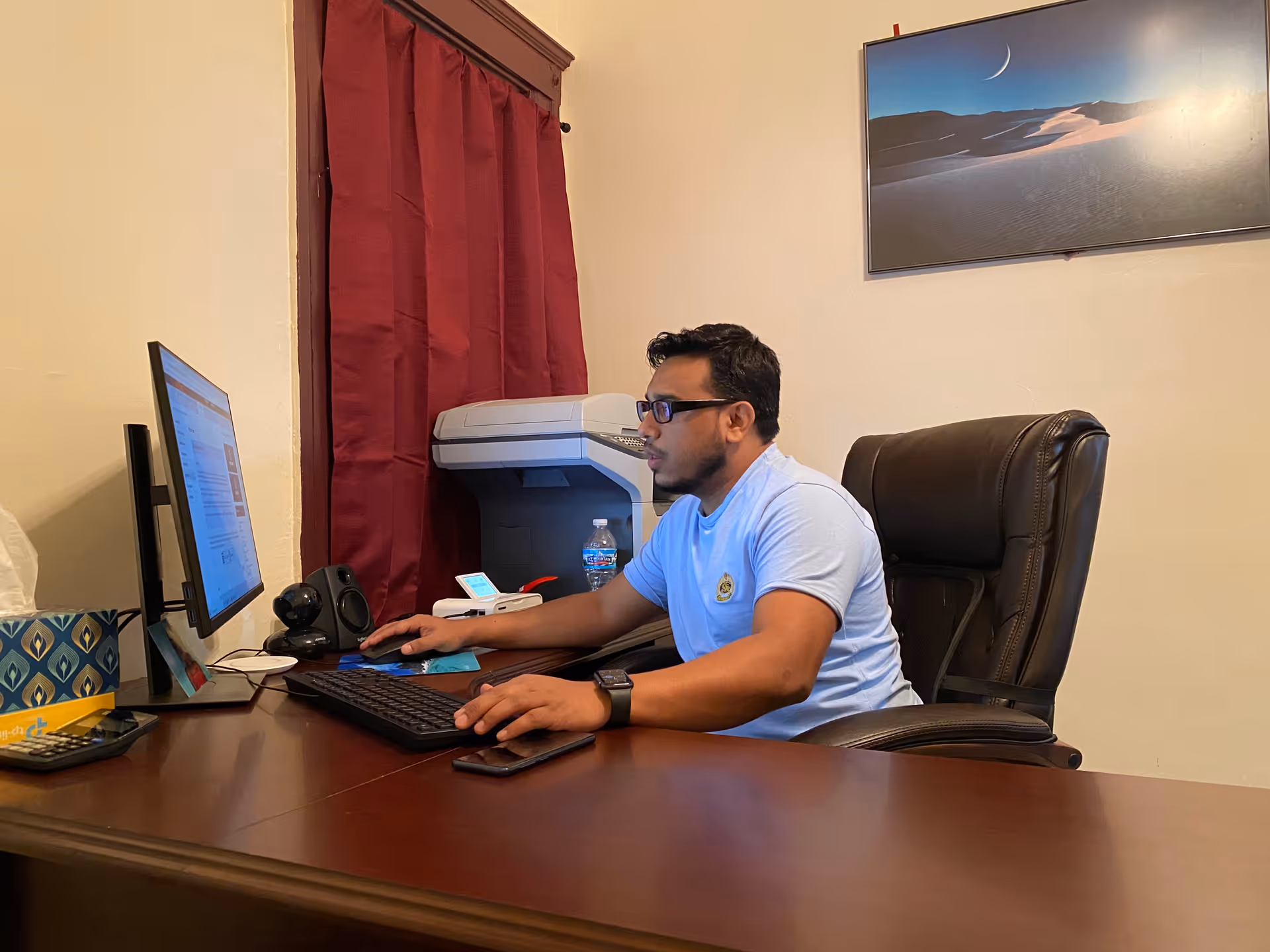 A man sits at a desk in an office, working on a computer.
