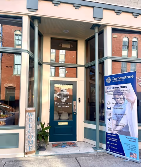 Entrance to Cornerstone Caregiving building featuring blue door, welcome sign, and informational banner.