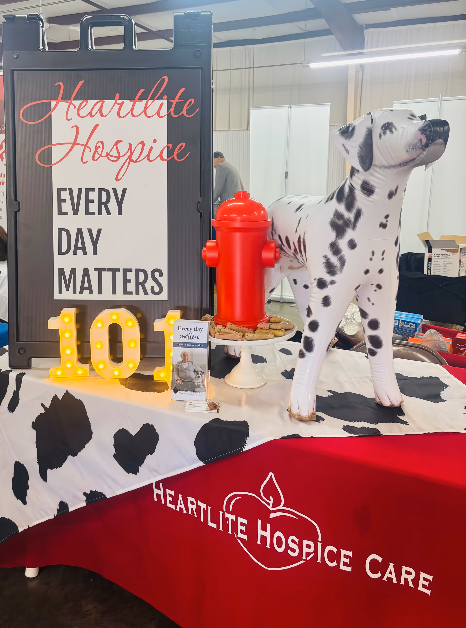Indoor hospice booth displaying Heartlite Hospice signage, a Dalmatian cutout, and a promotional table.