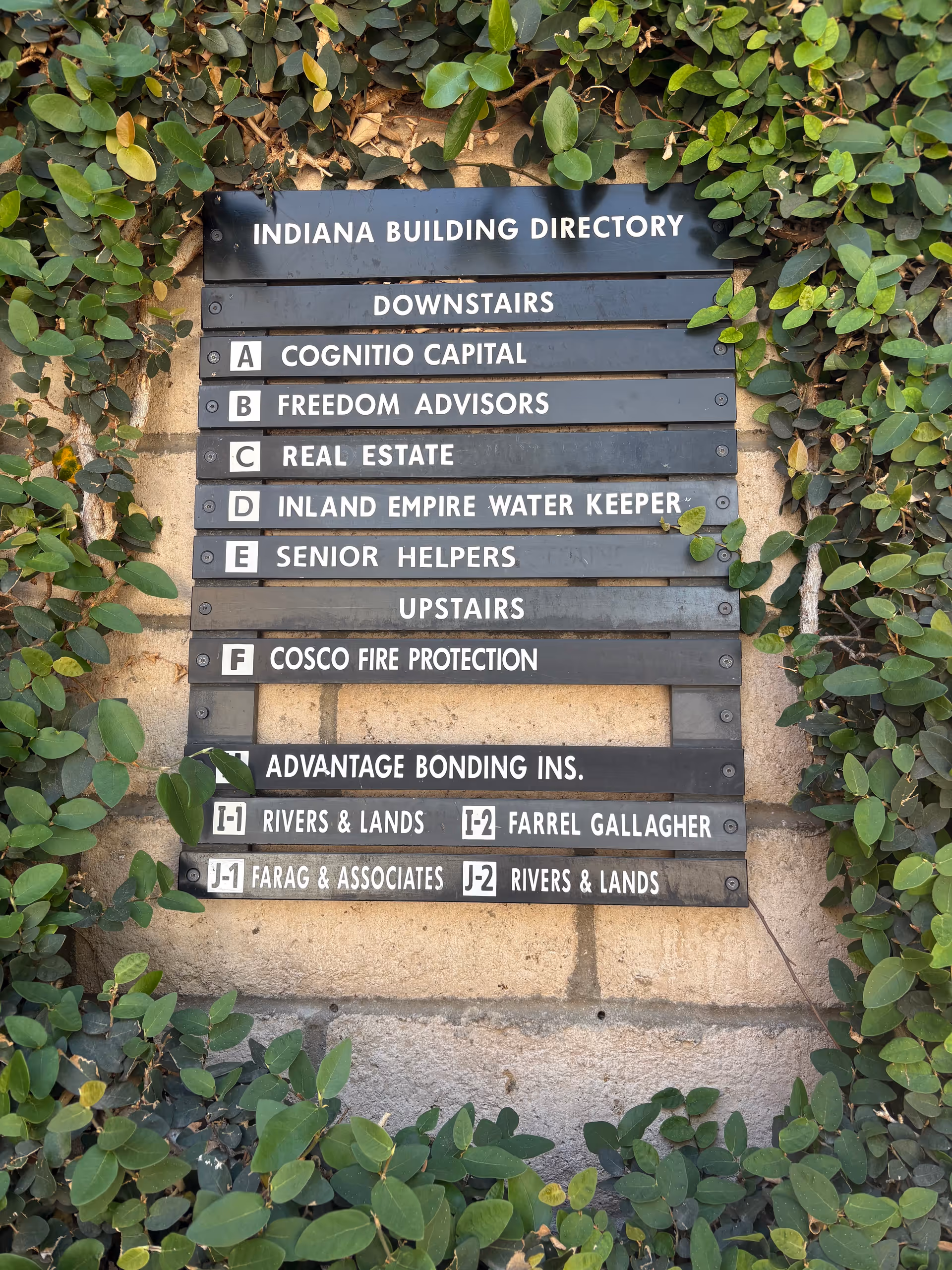 Outdoor wall-mounted building directory sign with ivy on brick wall, including Senior Helpers text.
