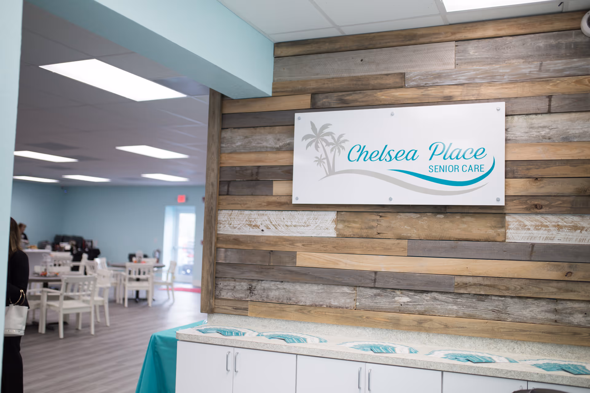 Interior of ActivAge at Chelsea Place with wood wall sign and dining area in background.
